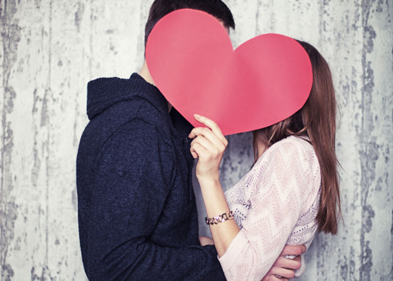 A couple kiss behind a paper heart