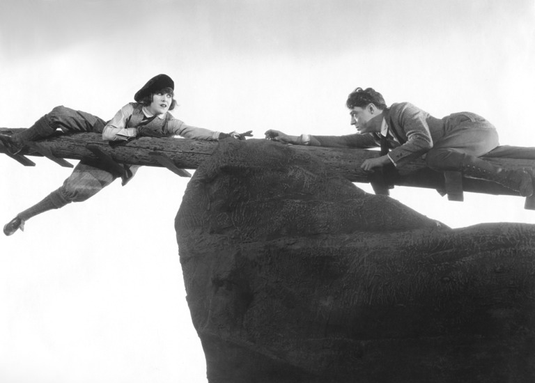 A man and woman hang precariously on a pole