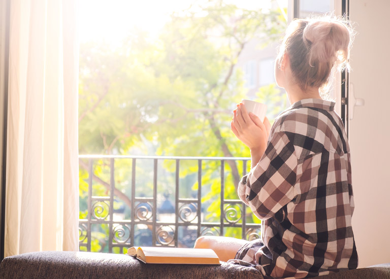 Woman looking out of a window holding a cup