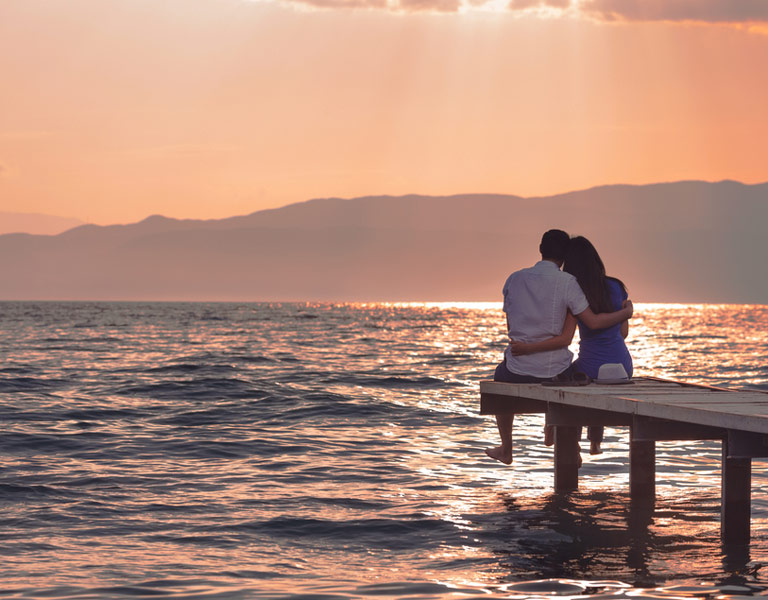 A couple sitting on a pier enjoying the sunset