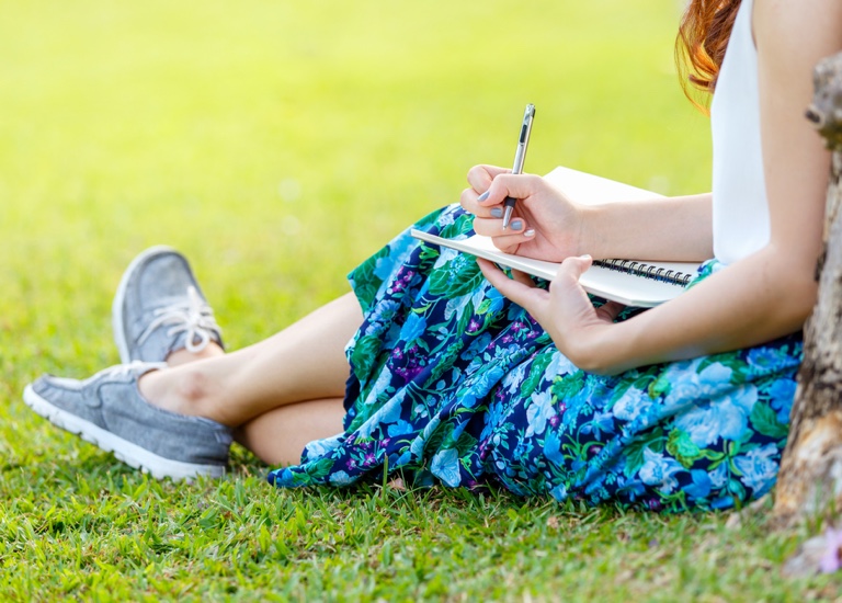Woman writing in a notepad whilst leaning on a tree