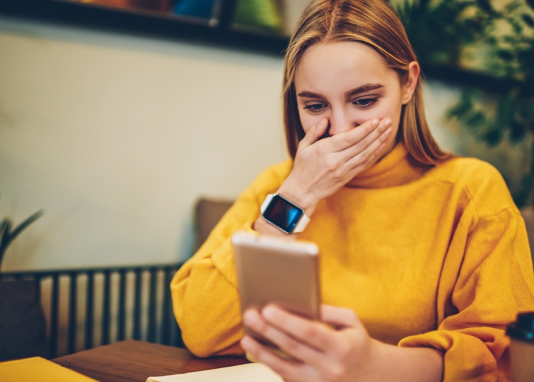 Woman looking at a smartphone with her hand covering her mouth