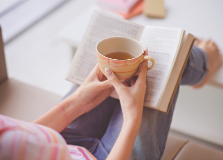 A woman reading a book quietly holding a cup of tea