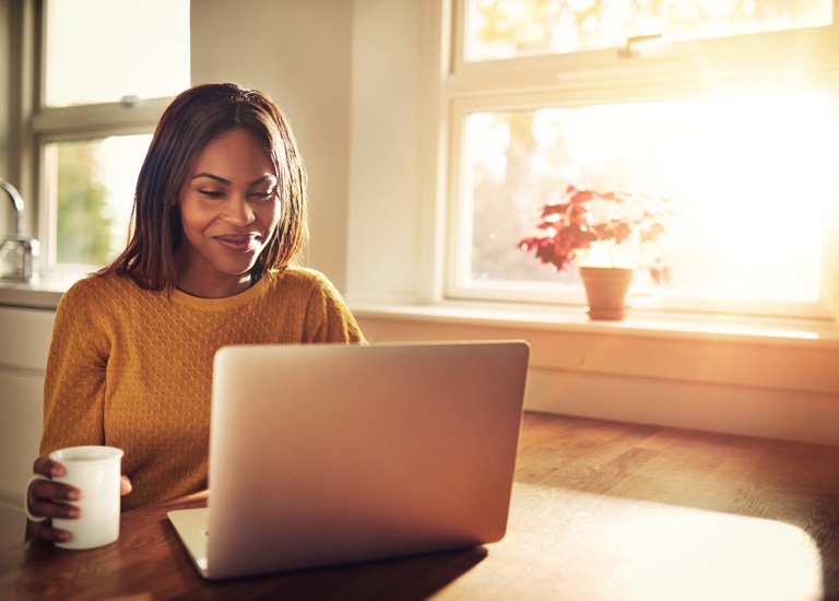 A happy woman sitting at a table working on a laptop