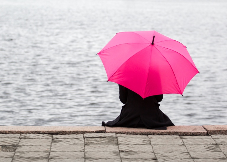 Woman holding umbrella looking out across the water