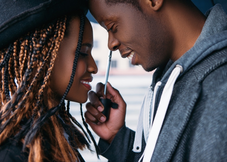 A couple stand very close to one another, underneath an umbrella