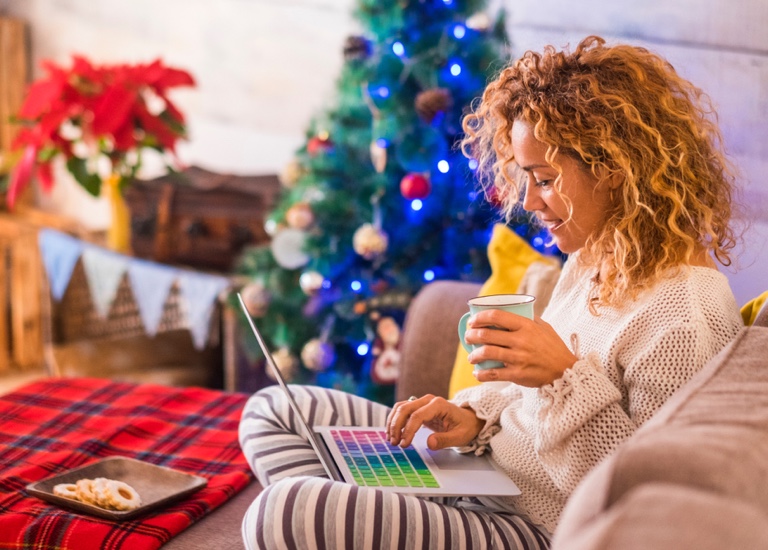 Woman in a Christmas setting on a laptop with a hot drink