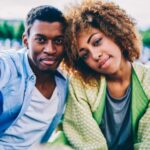 Close up portrait African American couple in love enjoying free time together resting outdoors, trendy dressed dark skinned hipster friends hugging while looking at camera during leisure on sunny day